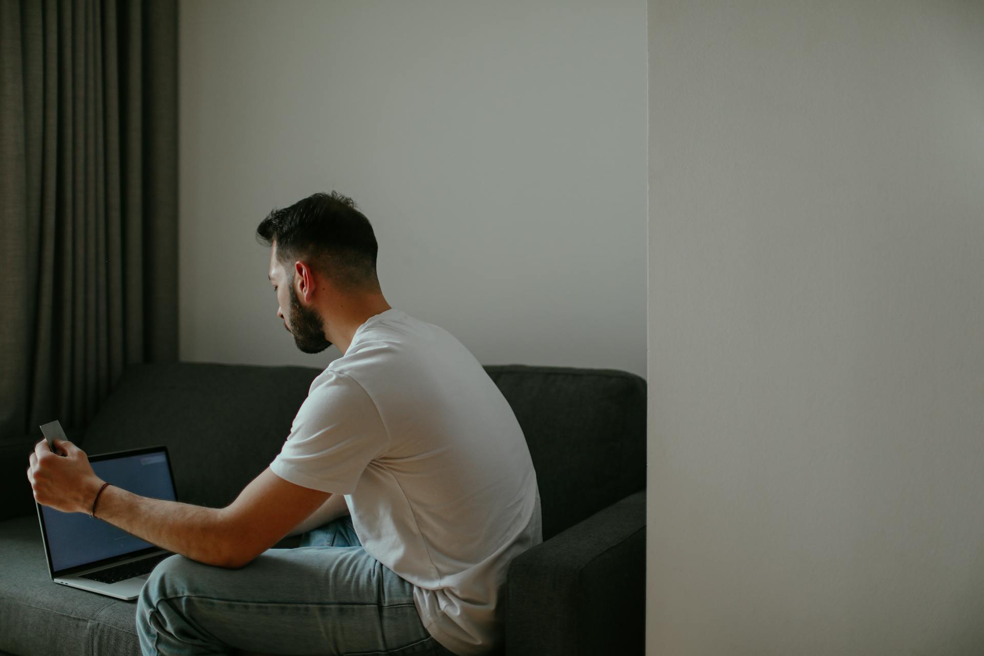 A man sitting on a sofa using a laptop for online shopping, holding a credit card.