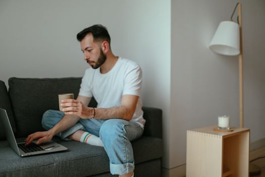 Cozy setting of a man using a laptop on a sofa, enjoying coffee indoors.