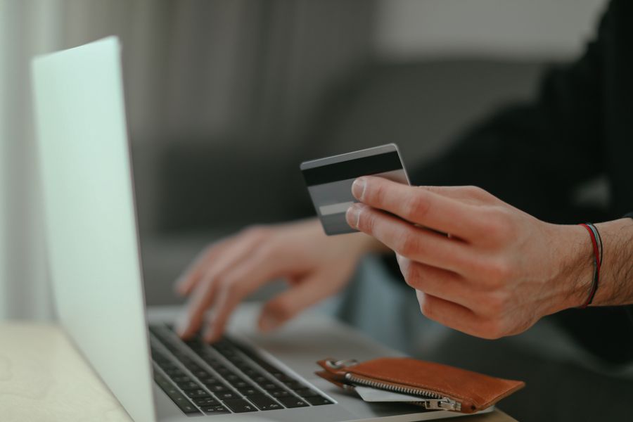 Close-up of a person holding a credit card while shopping online on a laptop.