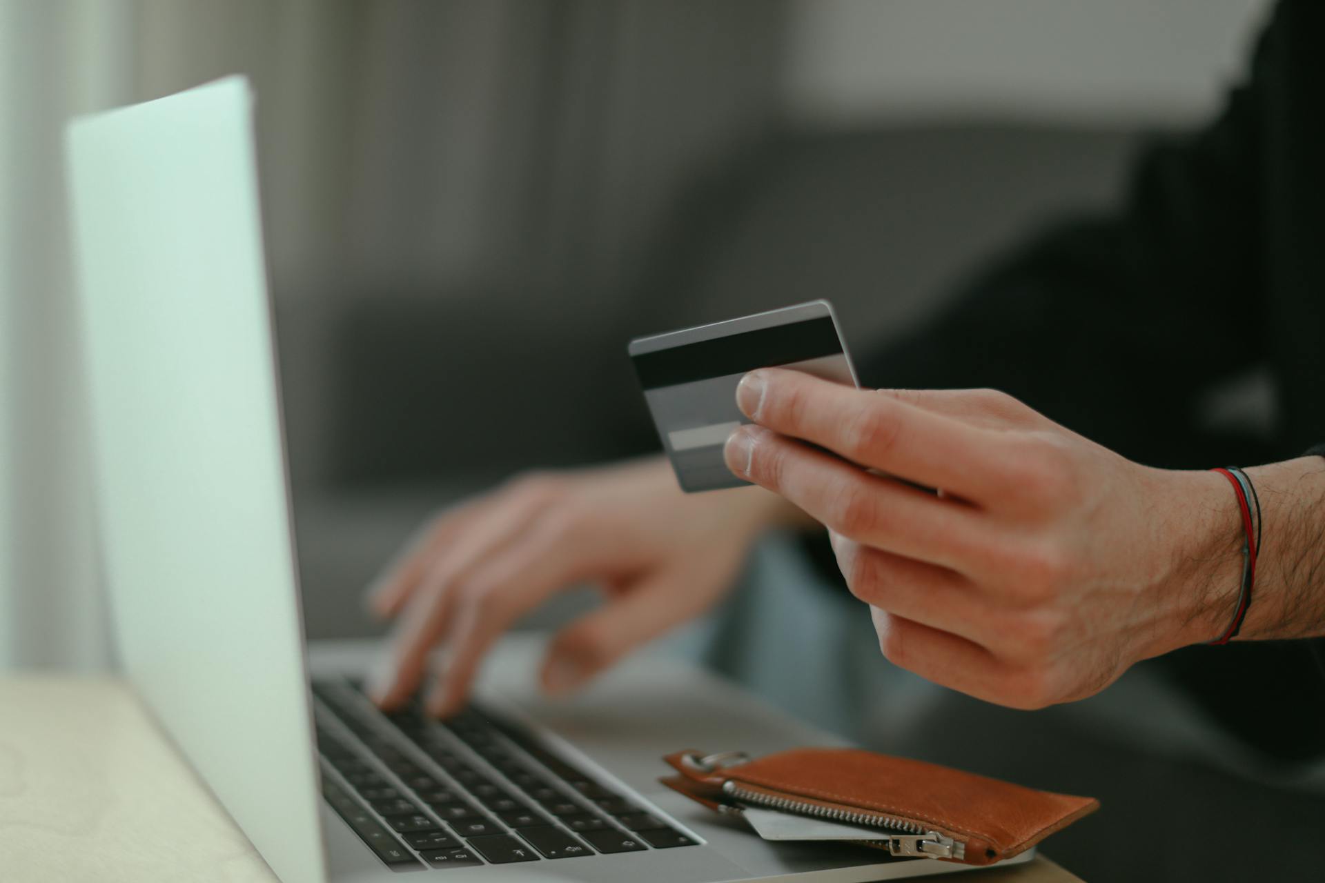 Close-up of a person holding a credit card while shopping online on a laptop.