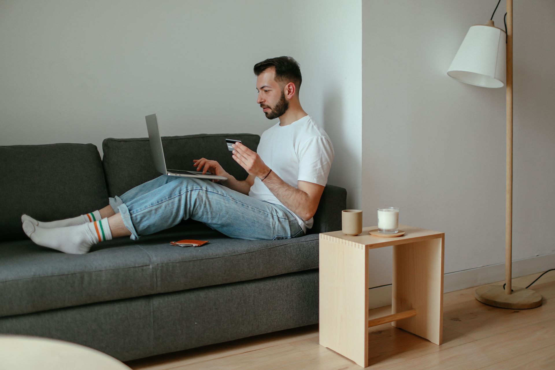 Adult man using laptop for online shopping on sofa, holding credit card.