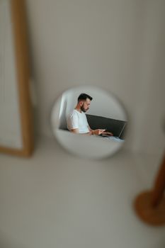 A man in a white shirt using a laptop, captured through a circular mirror, creating a unique focus.