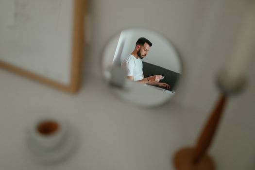 A man reflected in a mirror holding a credit card, engaged in online shopping from his living room.