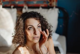 Woman applying skincare in a sunlit bedroom, embracing morning relaxation and self-care.