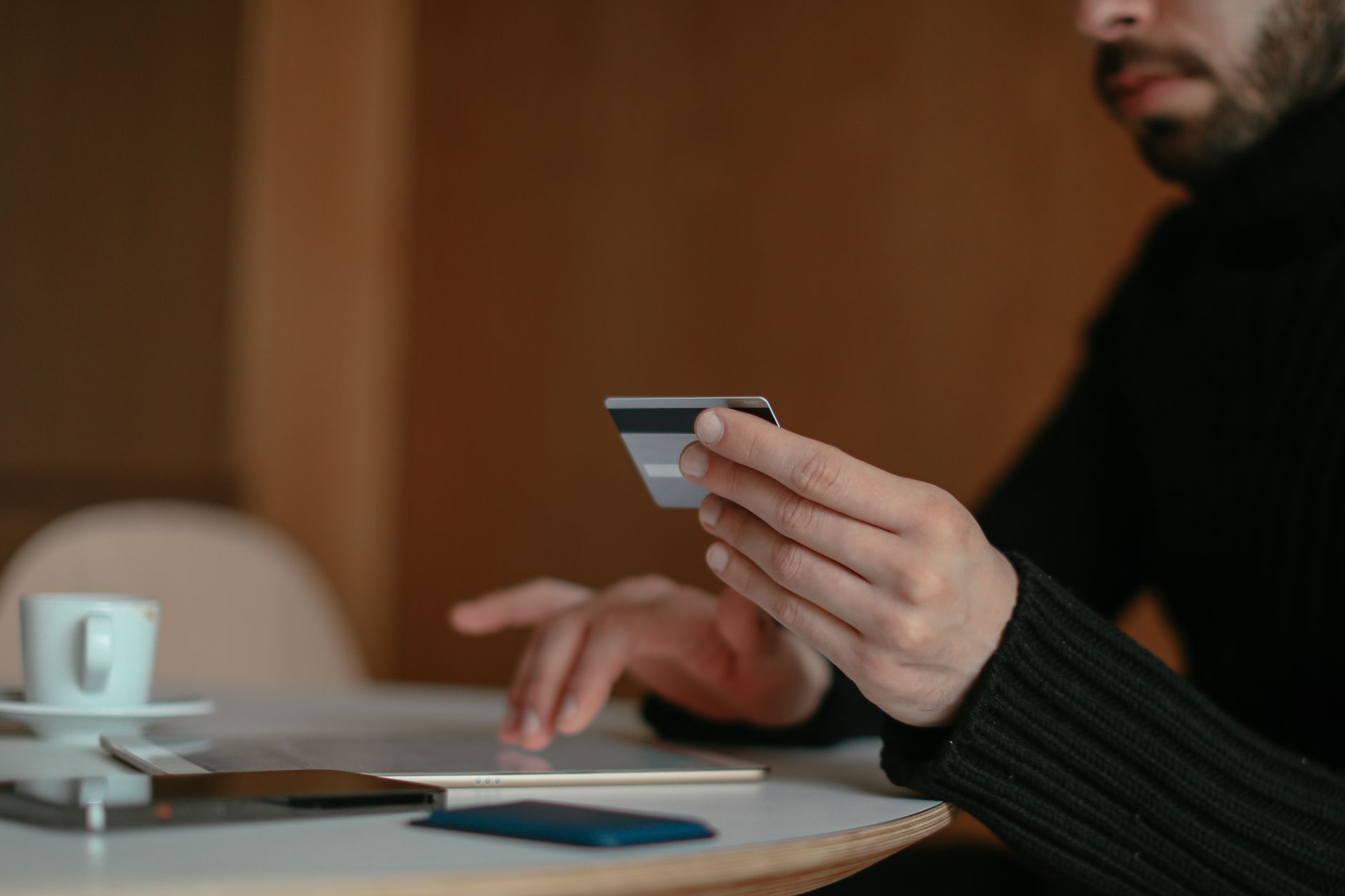 Close-up of a man holding a credit card and using a laptop for online shopping indoors.