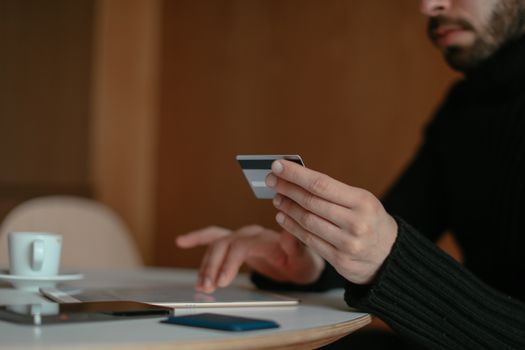 Close-up of a man holding a credit card and using a laptop for online shopping indoors.