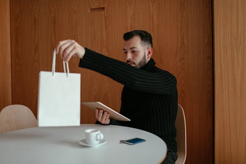 Man in Black Long Sleeve Shirt Holding White Paper Bag