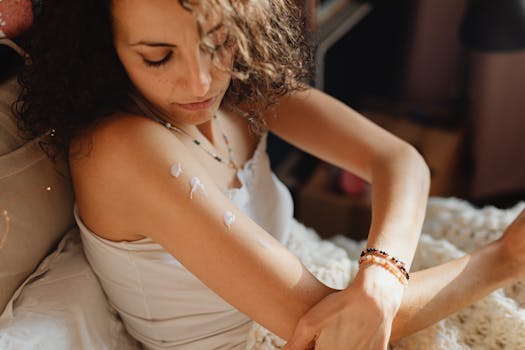 Young woman applying moisturizing cream on her arm in a cozy indoor setting.