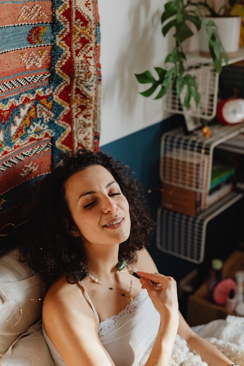 Woman Using Cosmetic Roller on Her Neck in a Bedroom with a Rug on a Wall