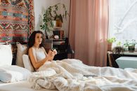 Woman relaxing on a bed with cozy blankets, enjoying a calm morning indoors.