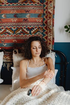 Woman with curly hair lying down in a bohemian-style room, applying cream.