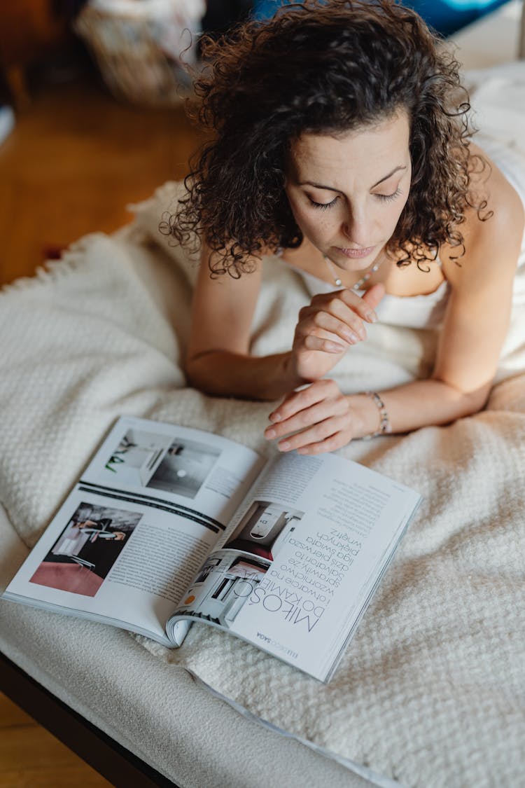 Woman Lying On Front In Bed Looking At A Magazine