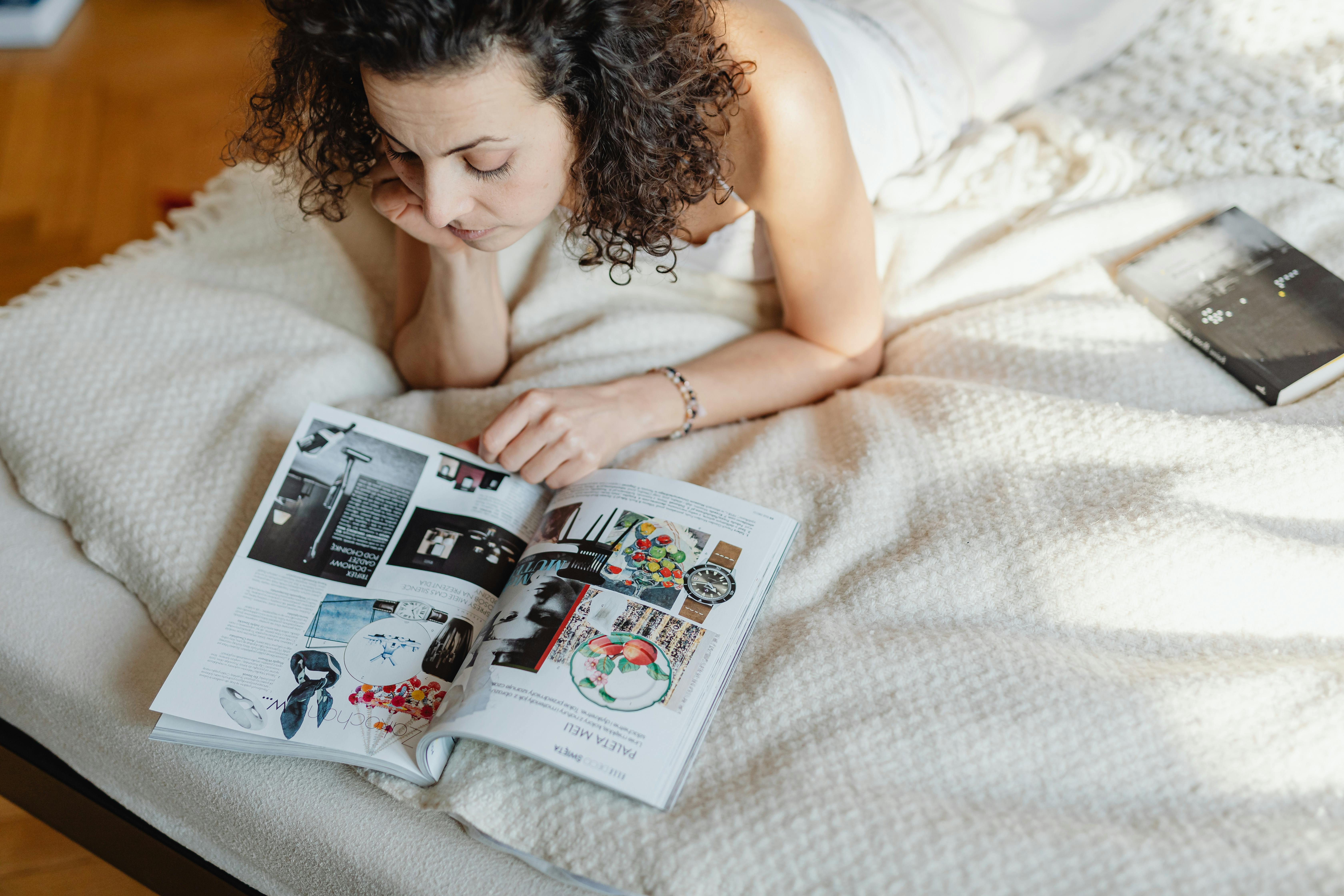 A woman lies in bed reading a magazine, enjoying a cozy and relaxed atmosphere.