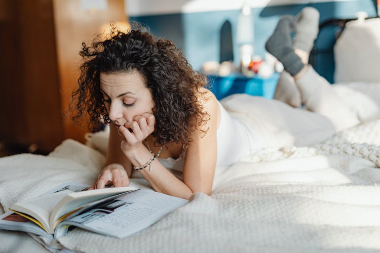 Woman Lying On Front In Bed Looking At A Magazine