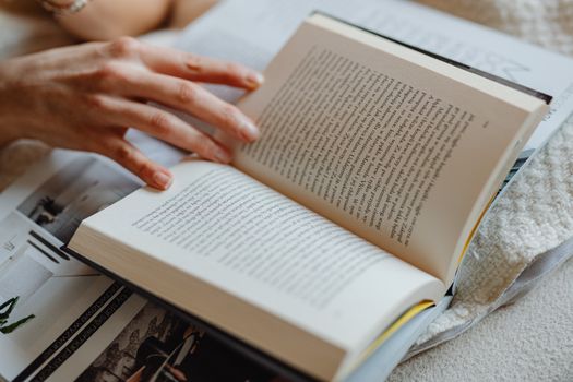 A person flipping through an open book, showcasing detailed text and a cozy indoor setting.