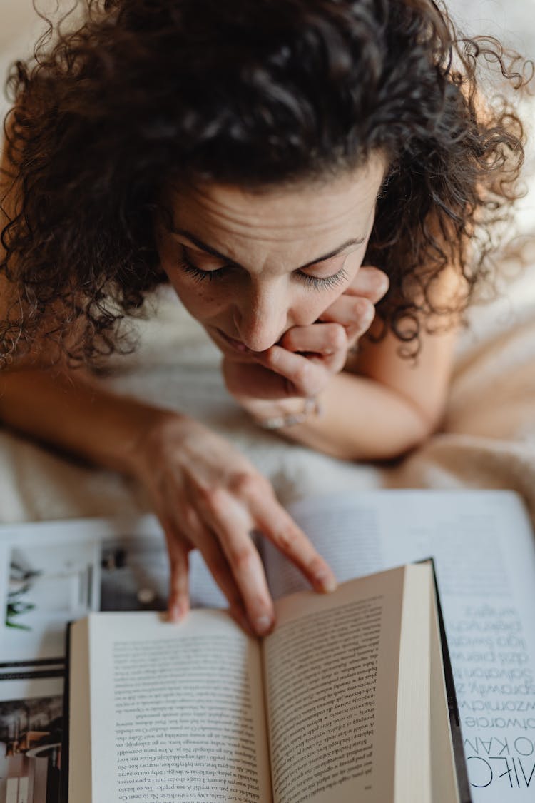 Woman Lying On Front In Bed Reading A Book