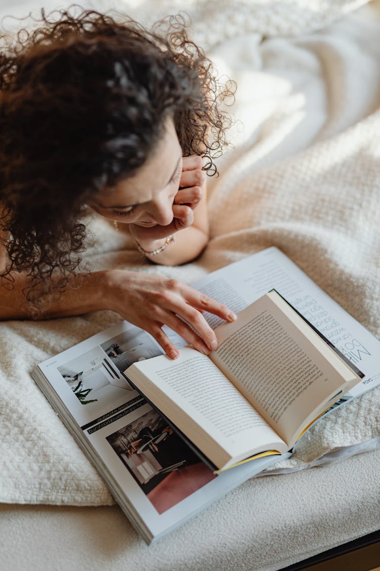 Woman Lying On Front In Bed Reading A Book