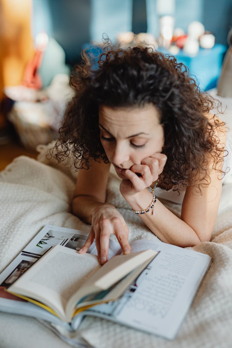 Woman Lying On Front In Bed Reading A Book