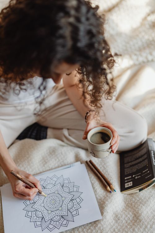 Free Woman enjoying a relaxing moment with a coloring book and coffee, enhancing creativity and mindfulness. Stock Photo