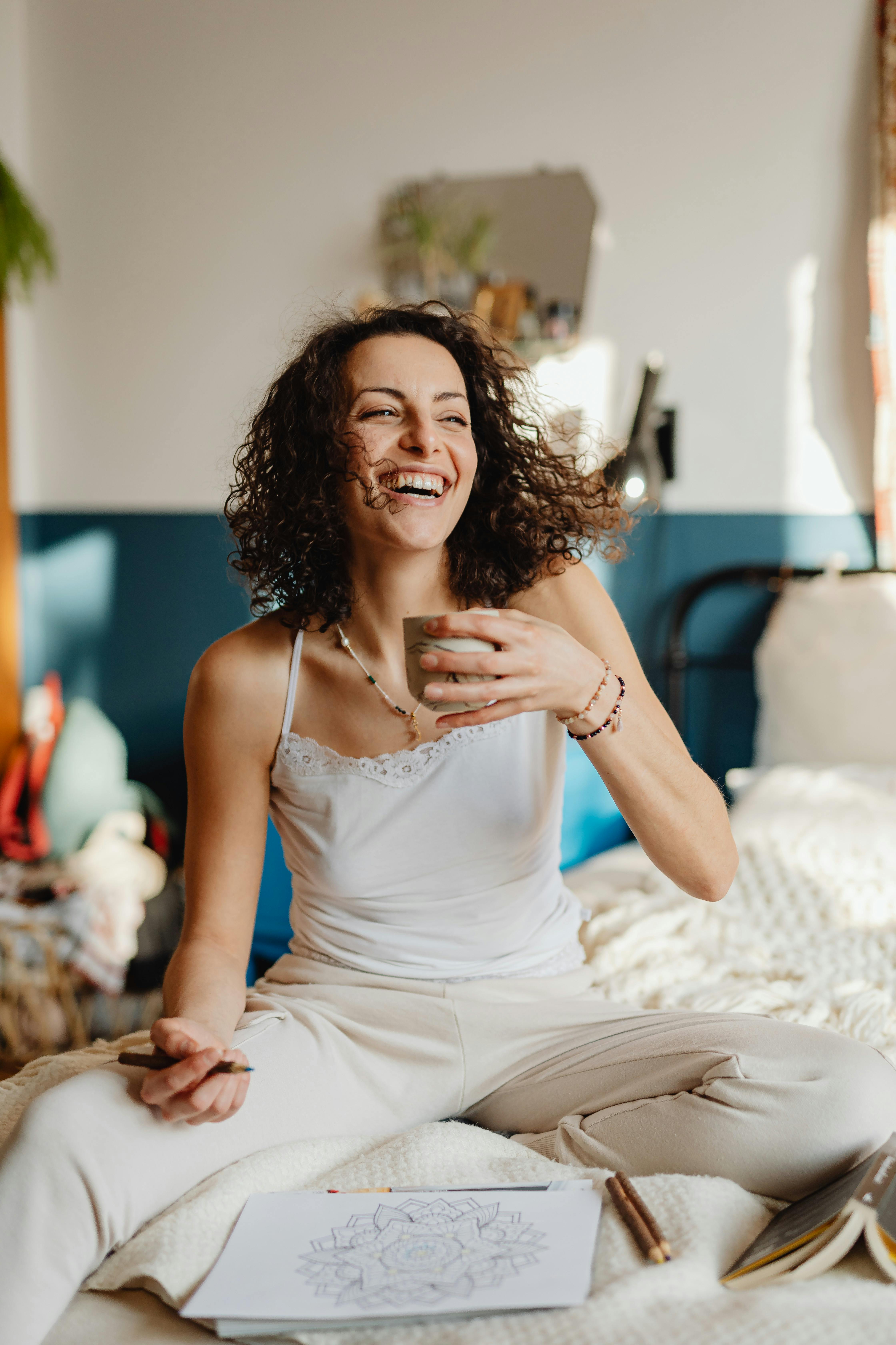 a woman in white spaghetti strap dress sitting on bed