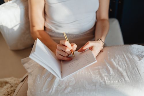 Free Close-up of a woman writing in a journal while sitting comfortably indoors. Stock Photo