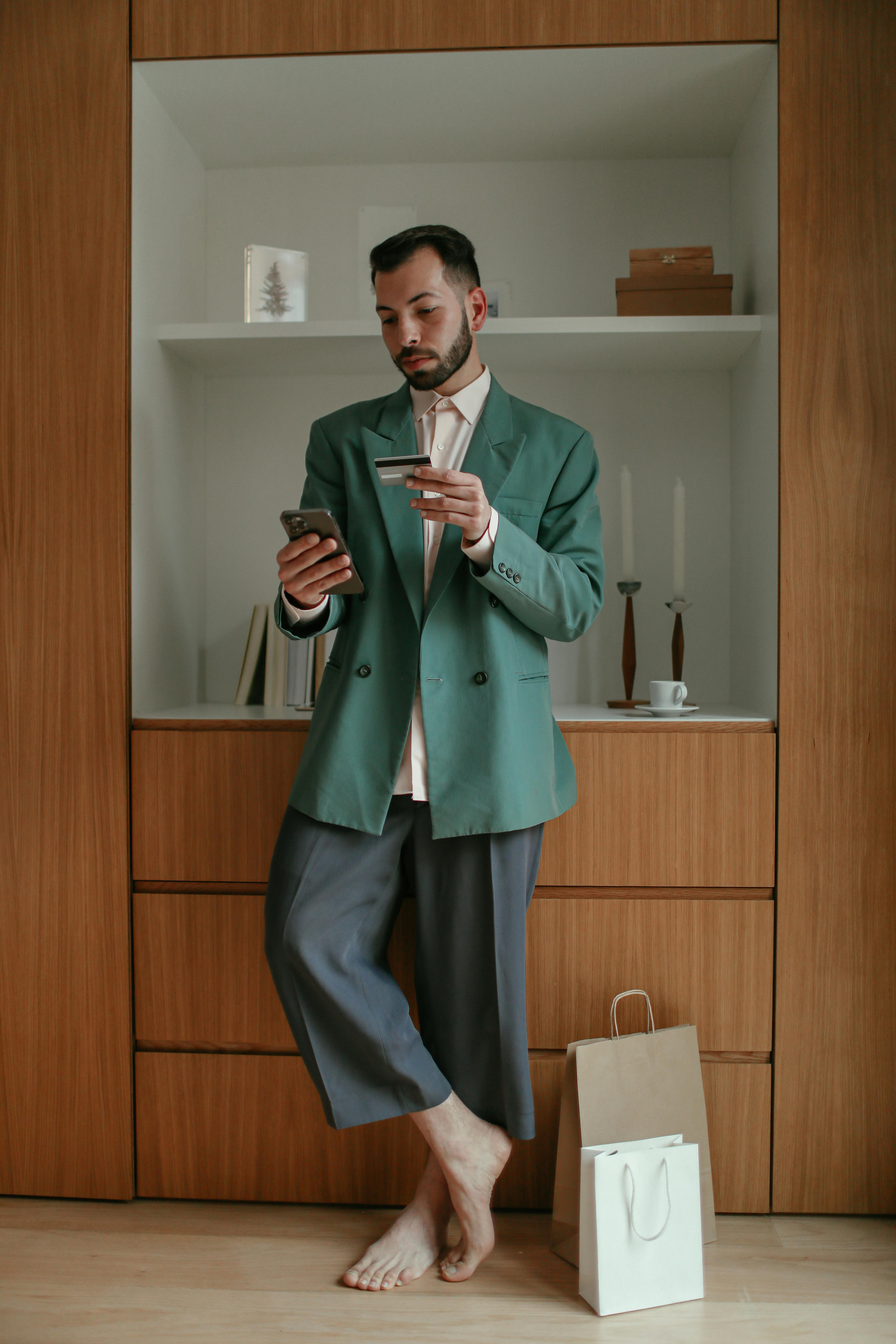 man in green suit holding his phone and bank card