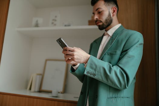 Elegant businessman in a teal suit using a smartphone indoors, showcasing technology in a modern setting.