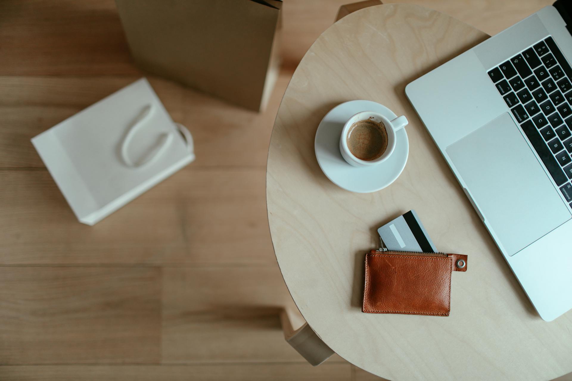 Minimalist top view of a workspace with coffee, laptop, and wallet on a wooden table.