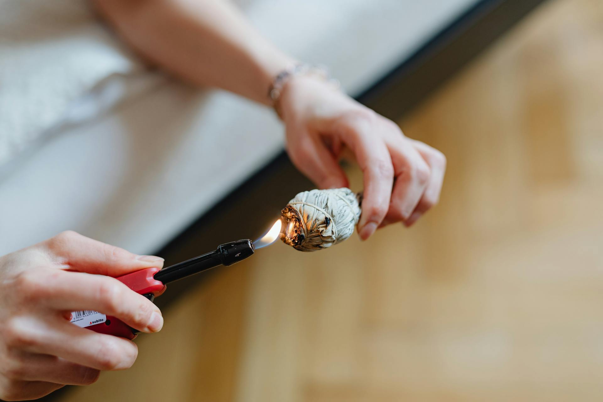 Hands lighting a sage smudge stick, symbolizing purification and spiritual cleansing indoors.