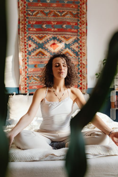 Free A woman meditates on a bed surrounded by bohemian decor and natural light, focusing on inner peace. Stock Photo