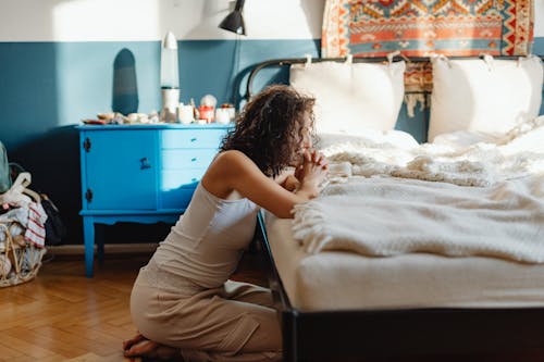 Free Woman in White Tank Top Praying on a Bed Stock Photo