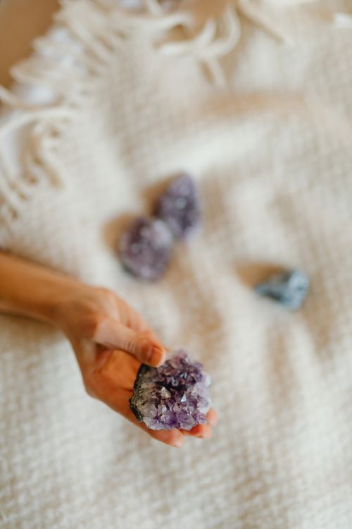 Free Close-up of a hand holding an amethyst crystal on a textured white blanket for holistic healing. Stock Photo