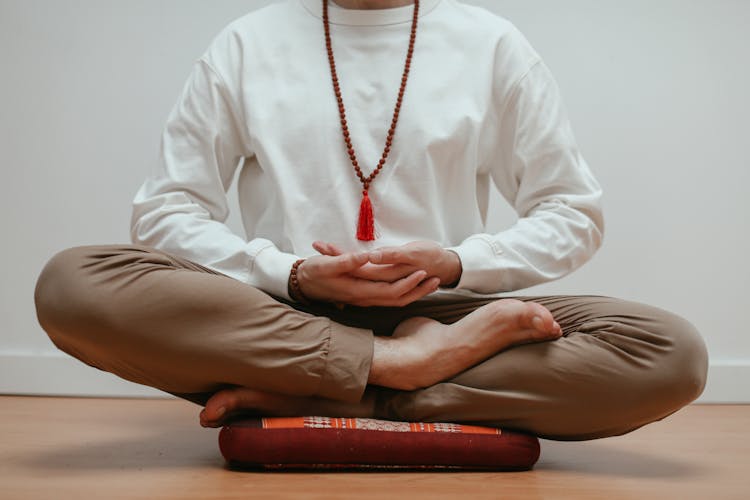 Man In White Long Sleeve Shirt And Brown Pants Sitting On Pillow Doing Yoga