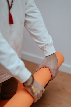 Close-up of hands rolling an orange yoga mat indoors, perfect for health and wellness themes.