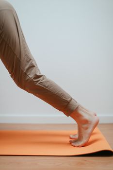 Detail of a person performing a yoga pose with bare feet on an orange mat indoors.