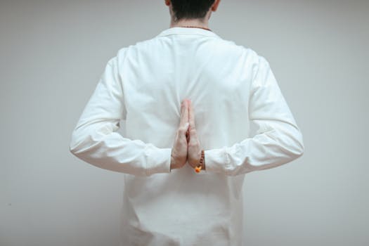 Back view of adult meditating in yoga pose with hands in reverse prayer position, embracing tranquility.