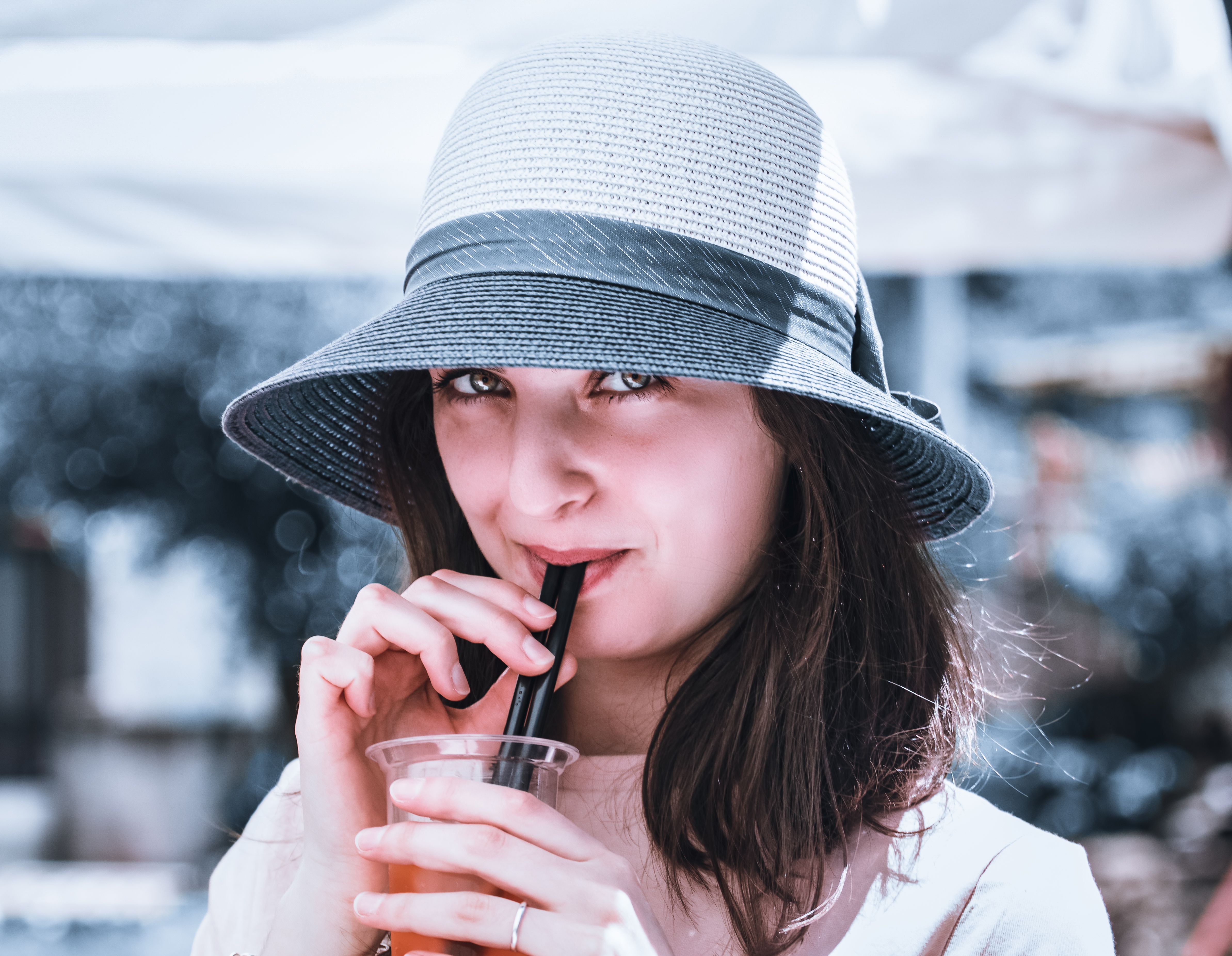 A woman in a stylish sun hat drinks from a straw on a sunny day, exuding elegance and relaxation.