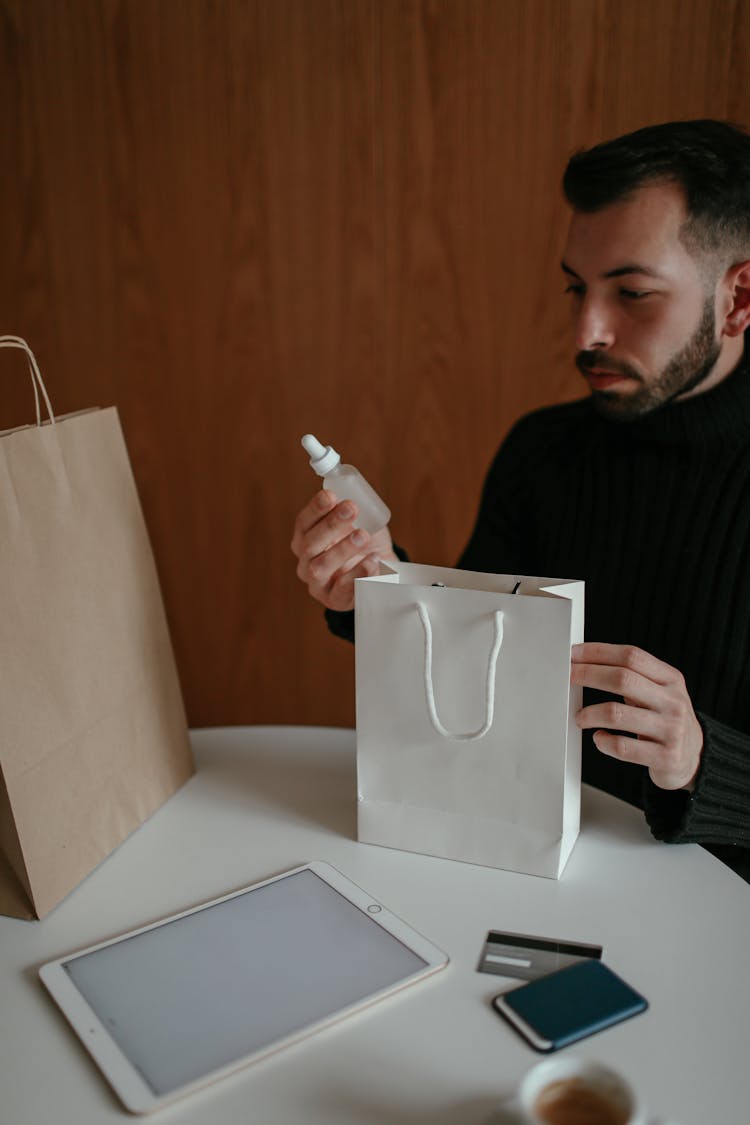 Serious Young Man Holding Skin Care Product After Online Shopping At Home