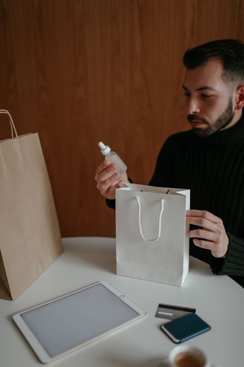 Free Crop self assured young bearded male buyer in casual clothes sitting at table and checking delivered purchases made via tablet with credit card at home Stock Photo