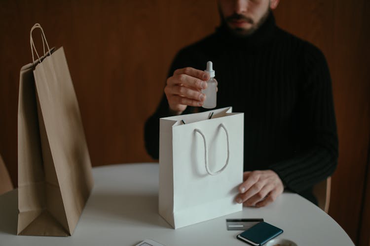 Focused Man Pulling Out Beauty Product From Shopping Bag At Table