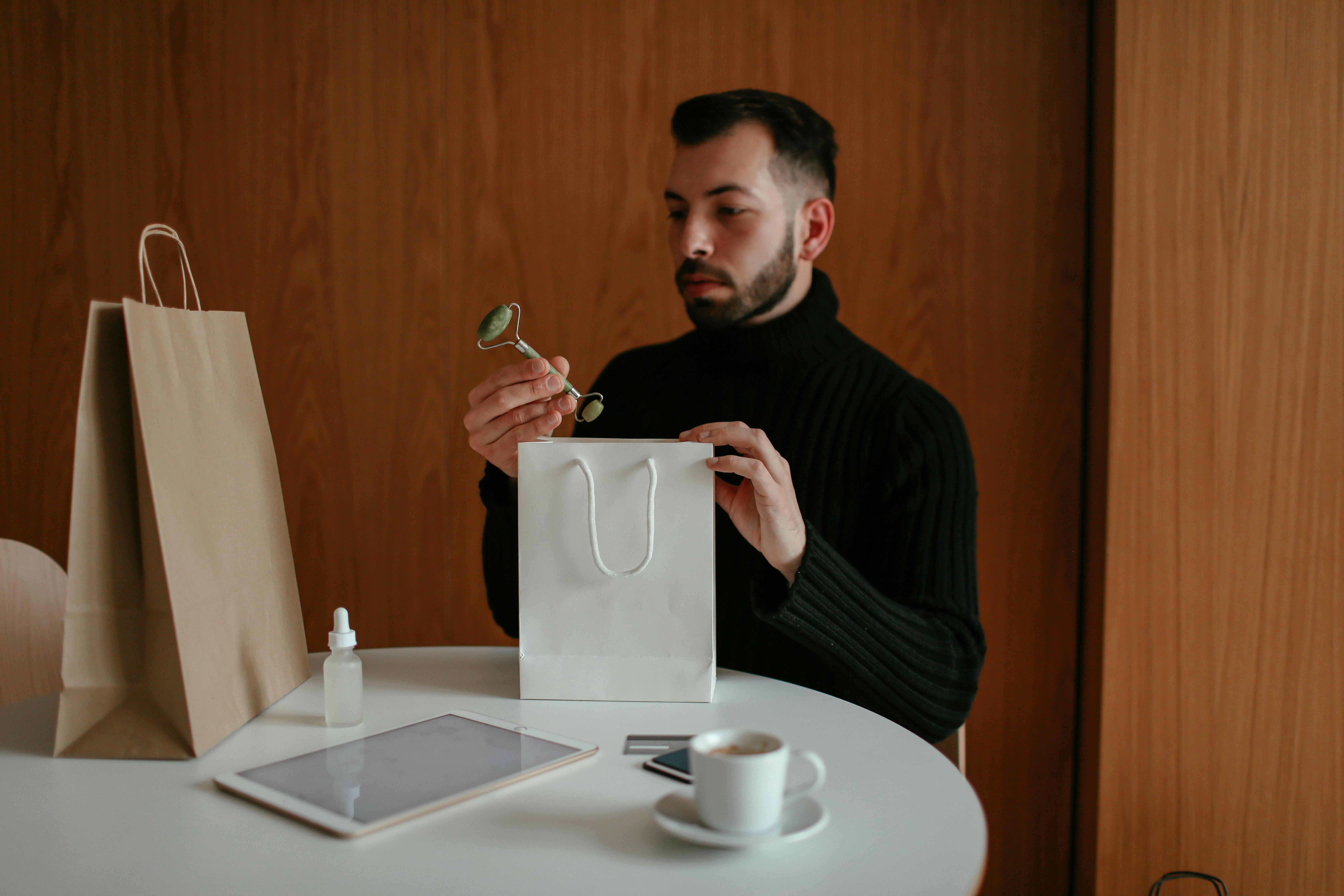 stylish man unpacking shopping bag with beauty products ordered with credit card