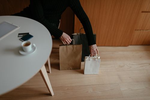Free From above of crop unrecognizable male shopaholic in casual clothes sitting at table with tablet and coffee and putting paper bags on floor after shopping Stock Photo
