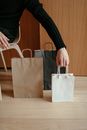 From above of crop faceless male putting various paper bags on wooden floor while sitting on chair at home after shopping