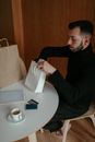Young man drinking coffee at table and checking purchases at home