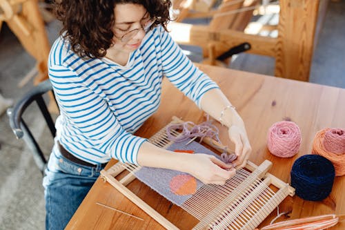 Woman Sitting at Table Weaving with Yarn Threads