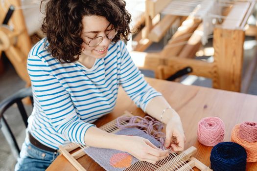A woman enthusiastically weaving yarn on a wooden loom, showcasing handmade craft.