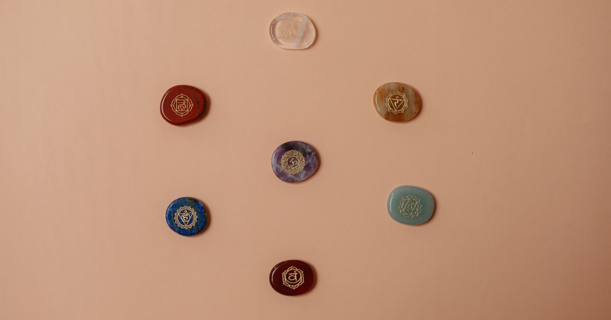 Flat lay of seven colorful chakra stones arranged in a row, representing the Destiny Matrix chakra energy line from root to crown