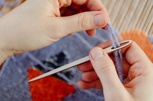 Hands of a Person Holding a Yarn on a Wooden Needle