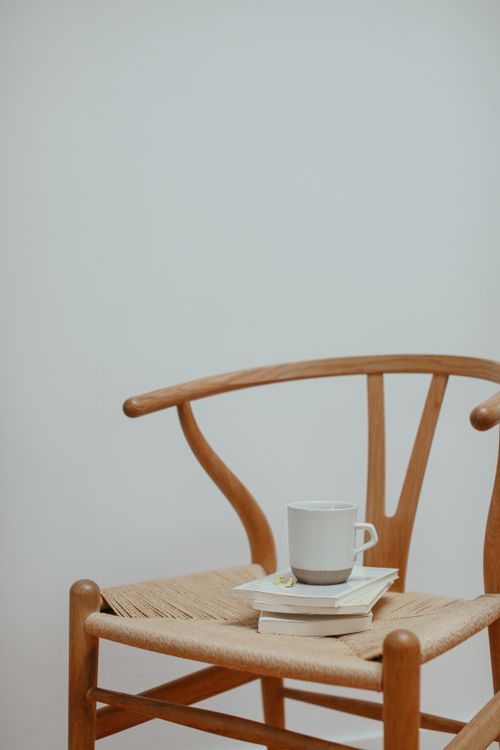 Free Minimalist scene of a wooden chair holding a coffee cup and books indoors. Stock Photo