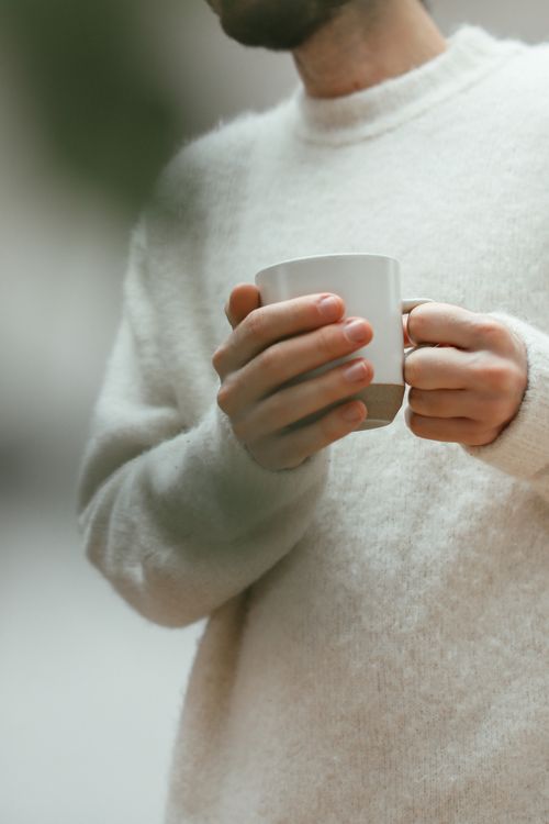 Free A person in a soft sweater enjoys a warm drink, capturing a serene and cozy moment. Stock Photo